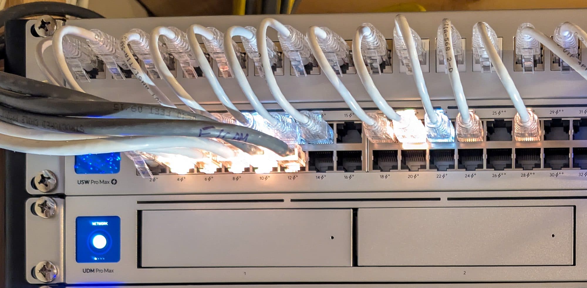 Detail — short patch leads from the patch panel into the UniFi USW Pro Max 48 PoE switch, with the UDM Pro Max gateway directly below