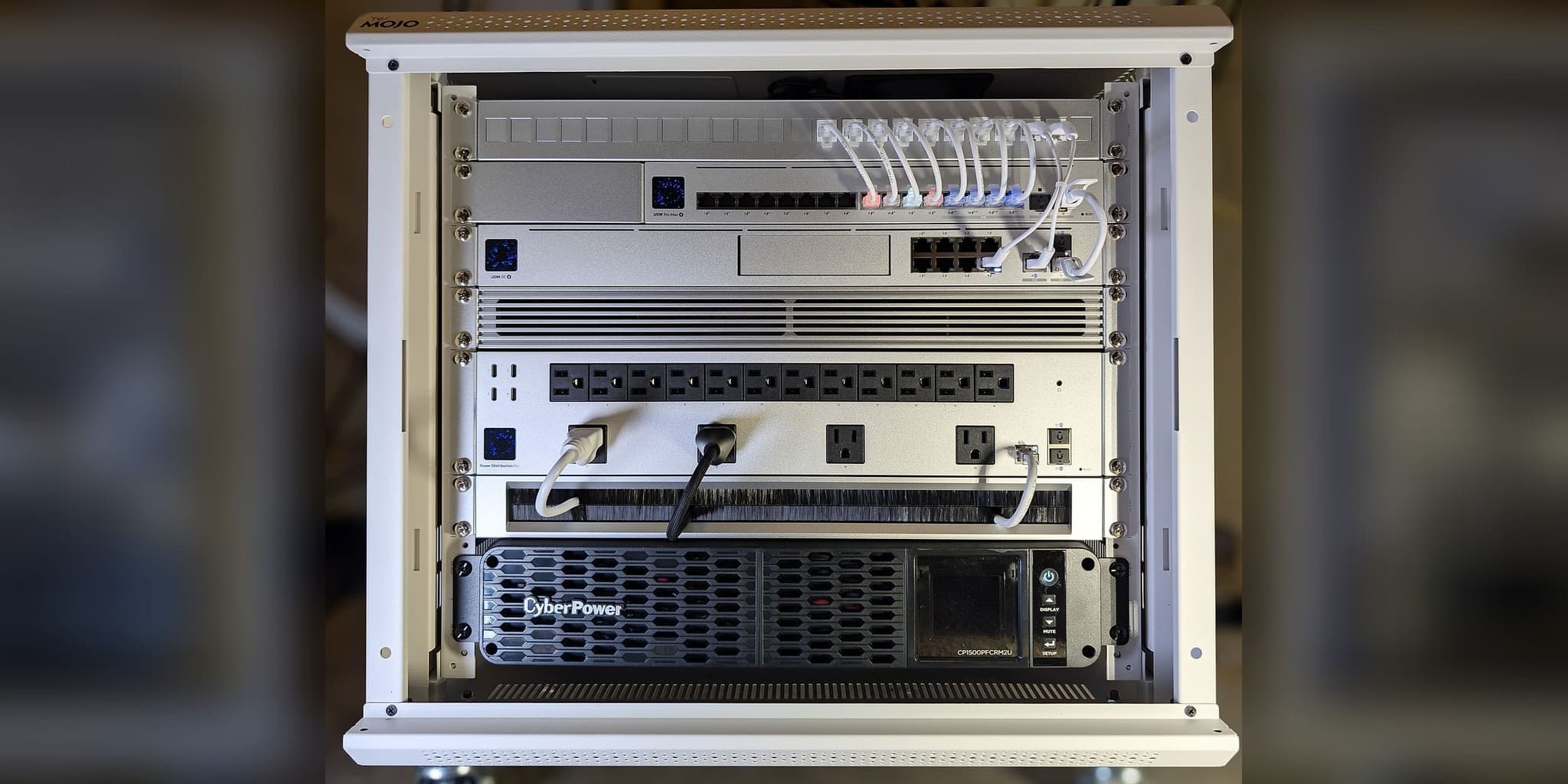 Commissioned wall-mount rack — labeled patch panel, USW Pro Max 16 PoE switch, UDM SE gateway, Power Distribution Pro, brush panel, and CyberPower pure sine-wave UPS