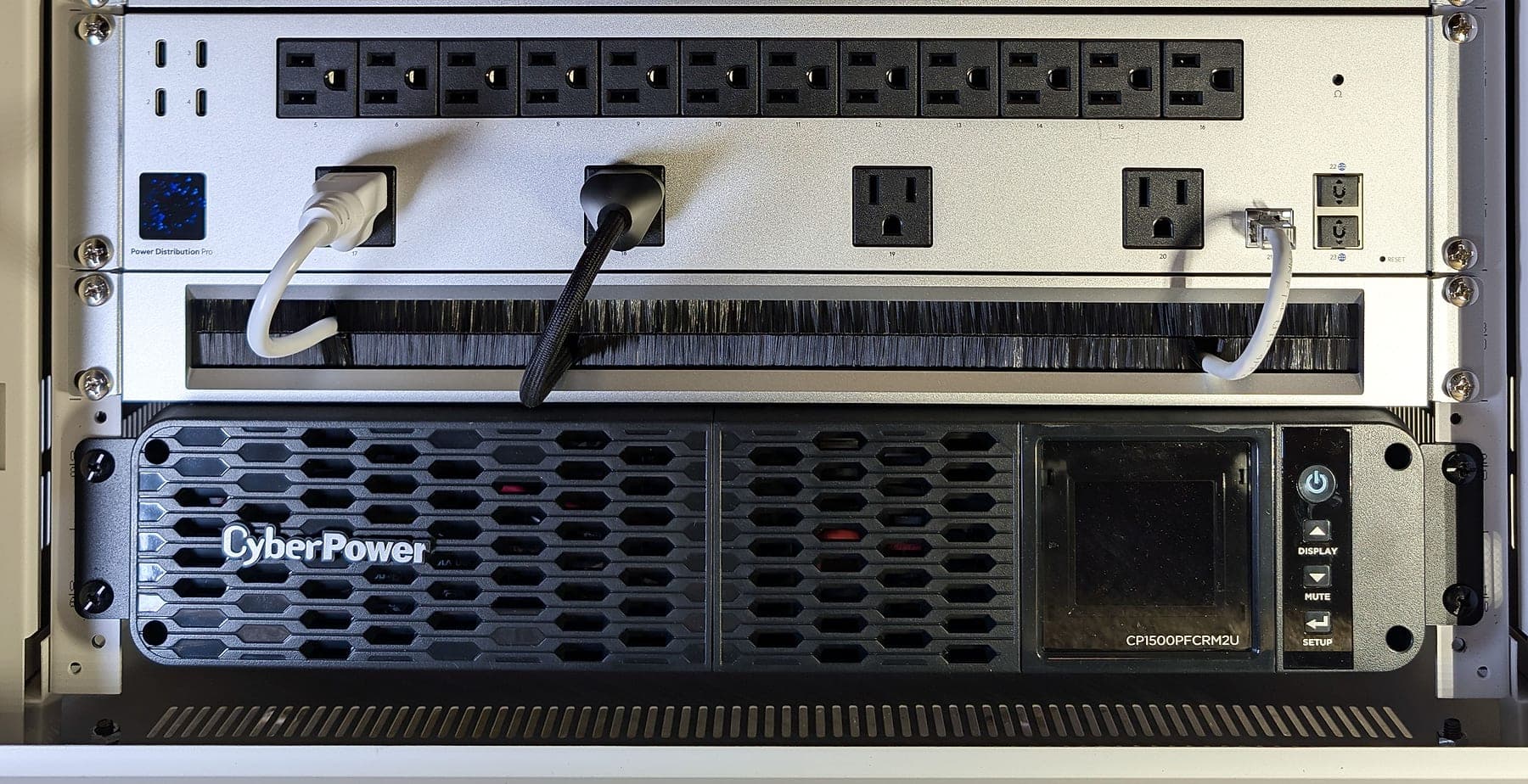 Detail — UniFi Power Distribution Pro with labeled outlets, brush panel, and CyberPower CP1500PFCRM2U pure sine-wave UPS