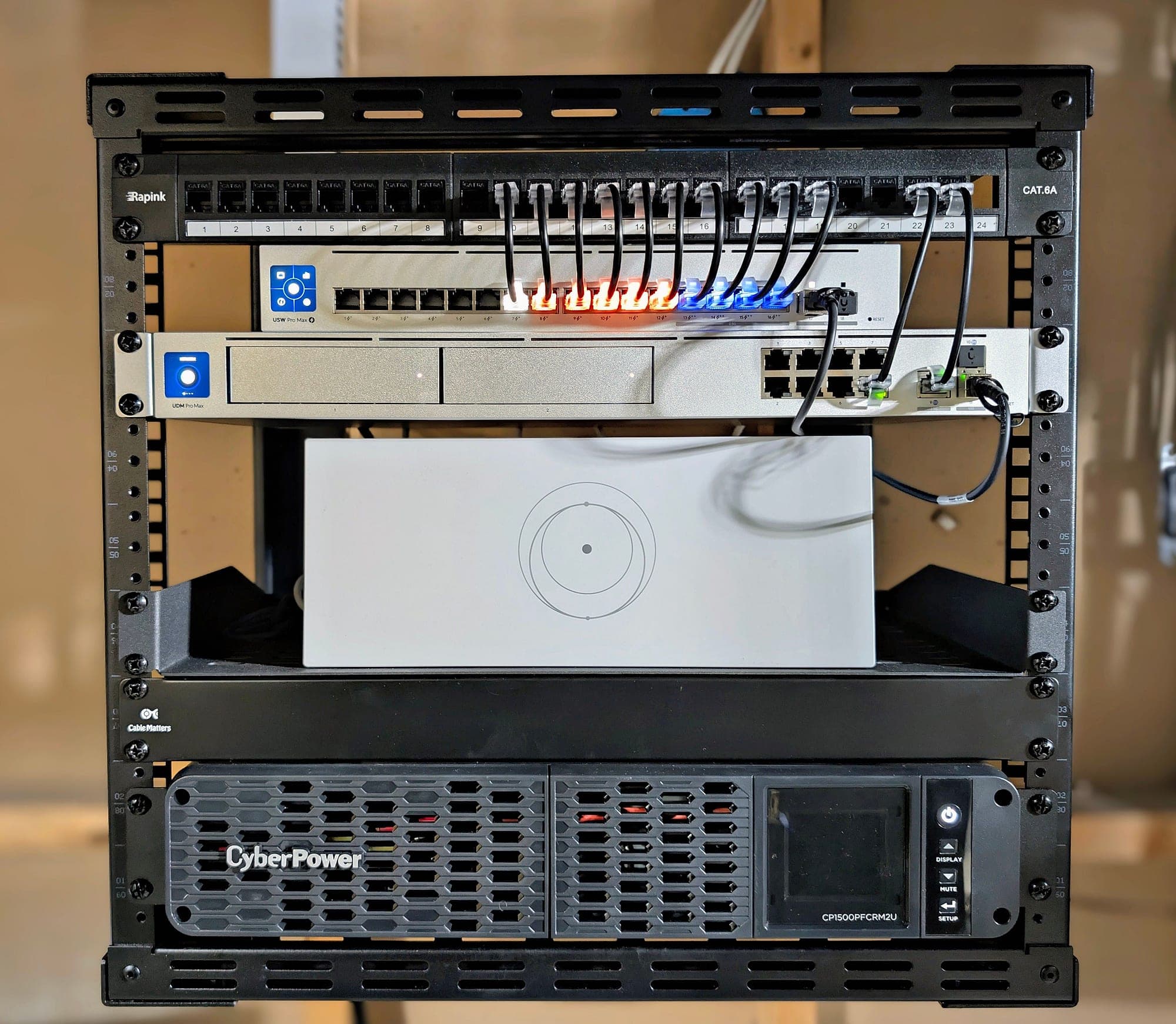 Open-frame rack detail — patch leads dressed from the panel to the switch, UPS at the base