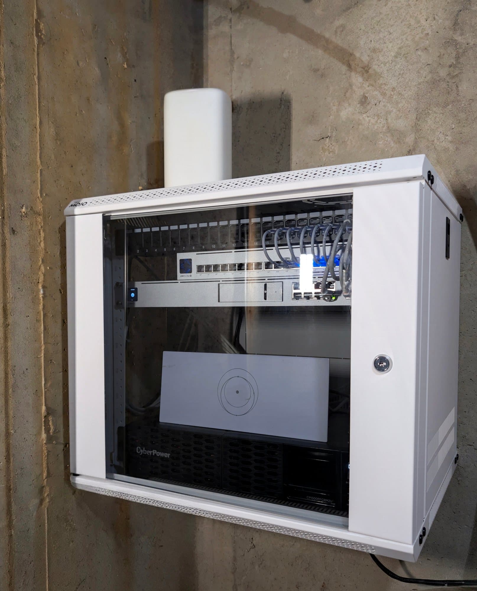 Lockable glass-door wall-mount enclosure — patch panel, USW Pro Max 16 PoE switch, UDM SE gateway, and CyberPower CP1500PFCRM2U pure sine-wave UPS