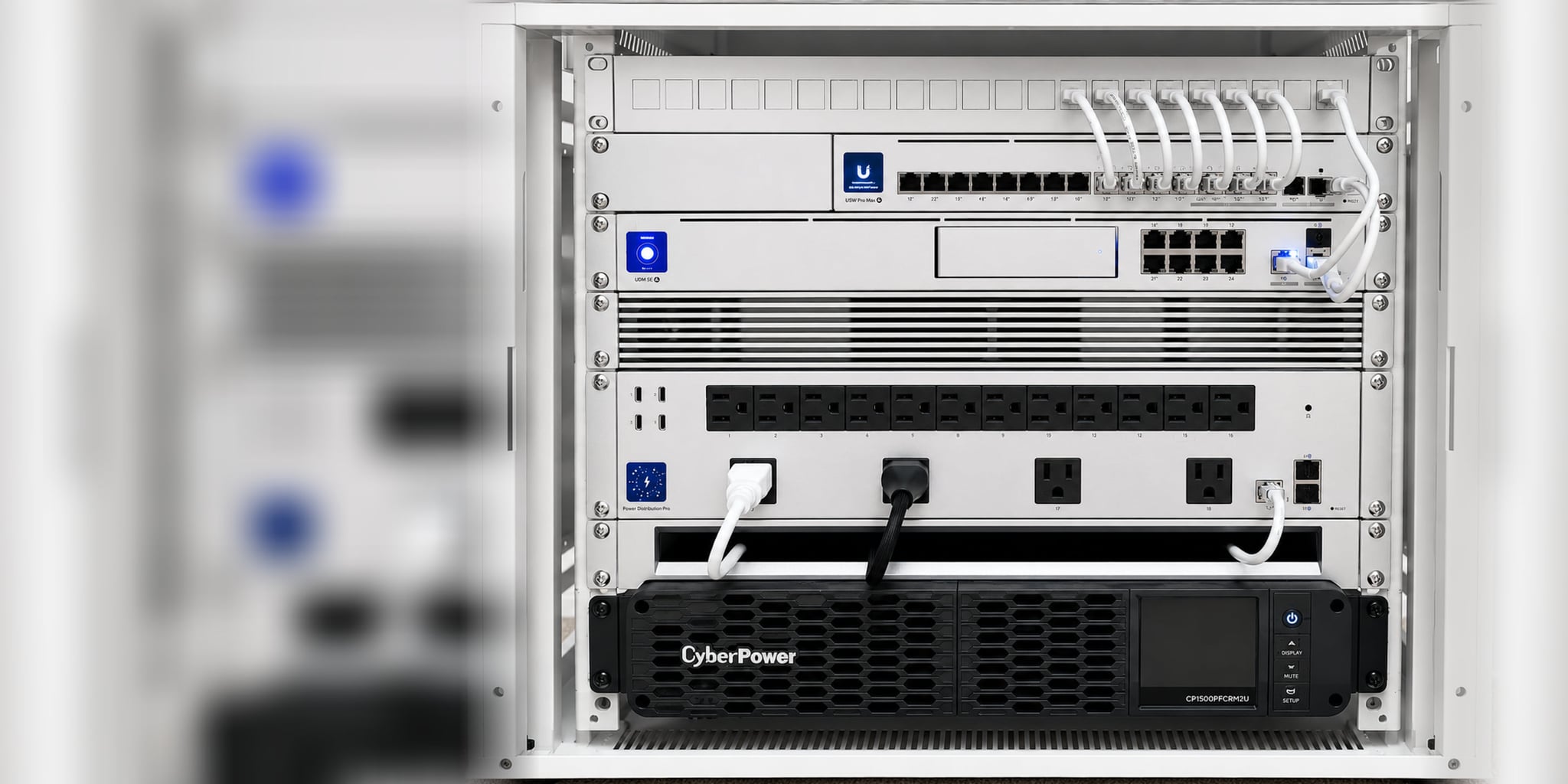 Commissioned executive network core — patch panel, UniFi USW Pro Max switch, UDM SE gateway, rack power distribution, and rack-mount UPS in a white enclosure