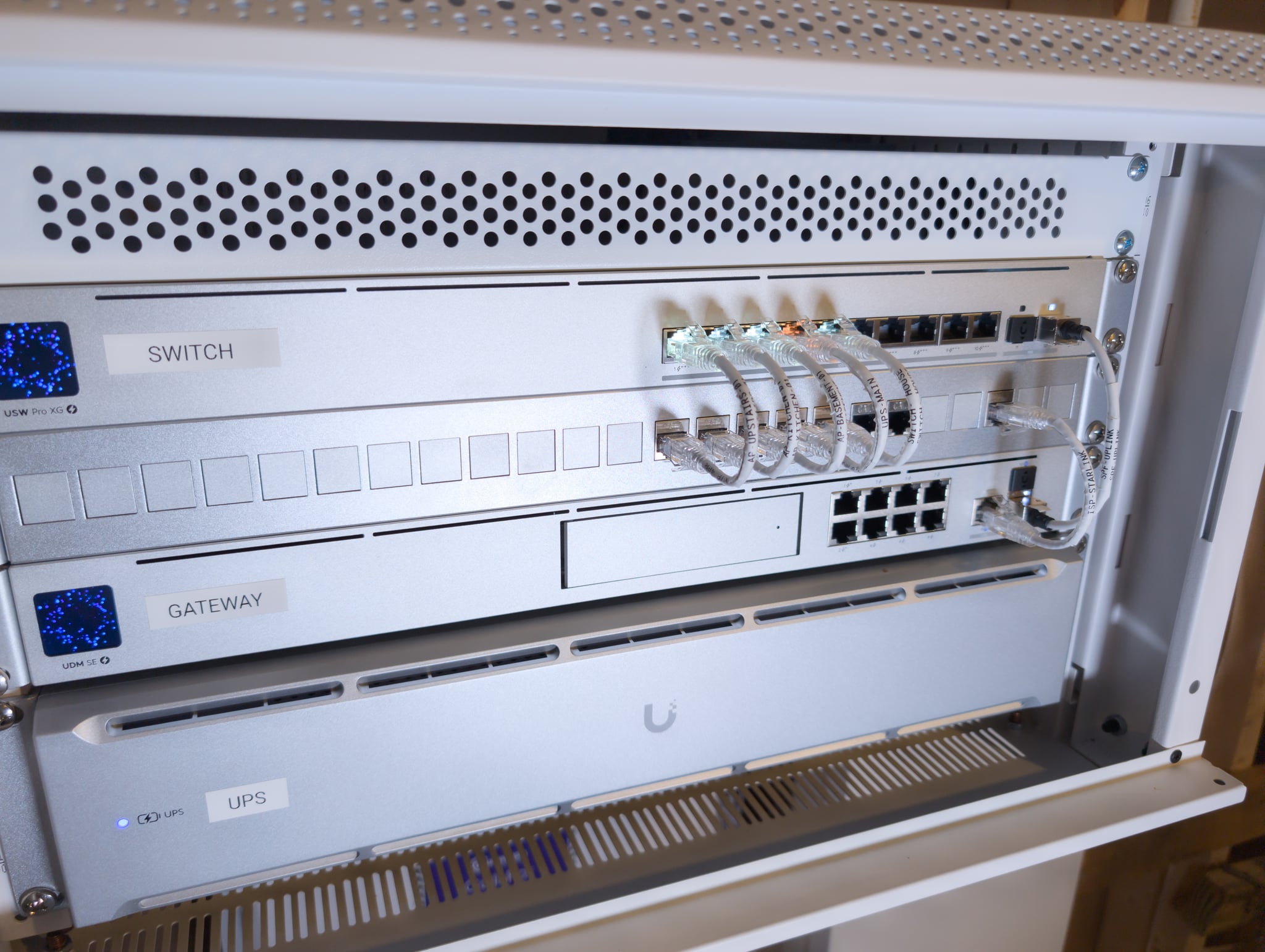 Rack-mounted UDM SE, USW Pro XG 10 PoE switch, and UPS 2U — all LEDs active, every device named and monitored