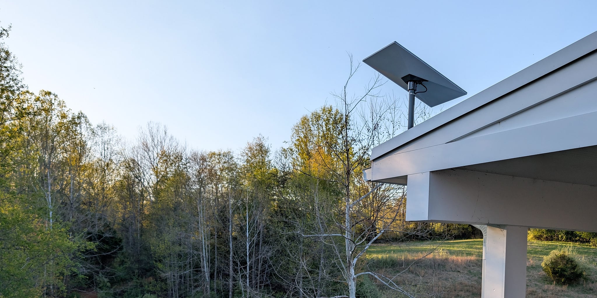 Starlink dish mounted at a pavilion roofline at dusk, with treeline and pasture beyond — a rural property served by satellite