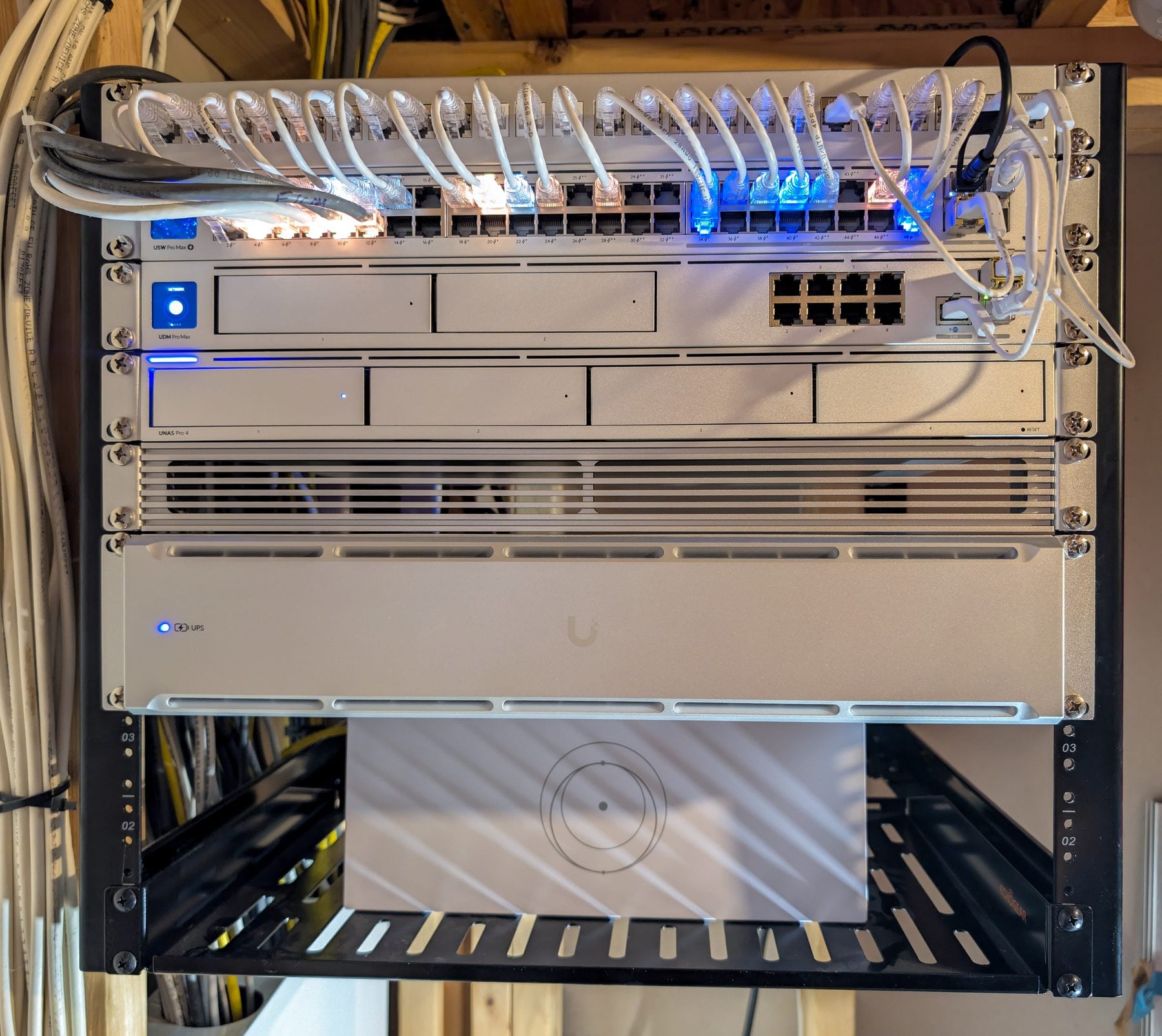 Wall-mounted open-frame network rack — patch panel, UniFi USW Pro Max 48 PoE switch, UDM Pro Max gateway, UNAS Pro 4 storage, vented panel, UniFi UPS 2U, and the Starlink router on the shelf below