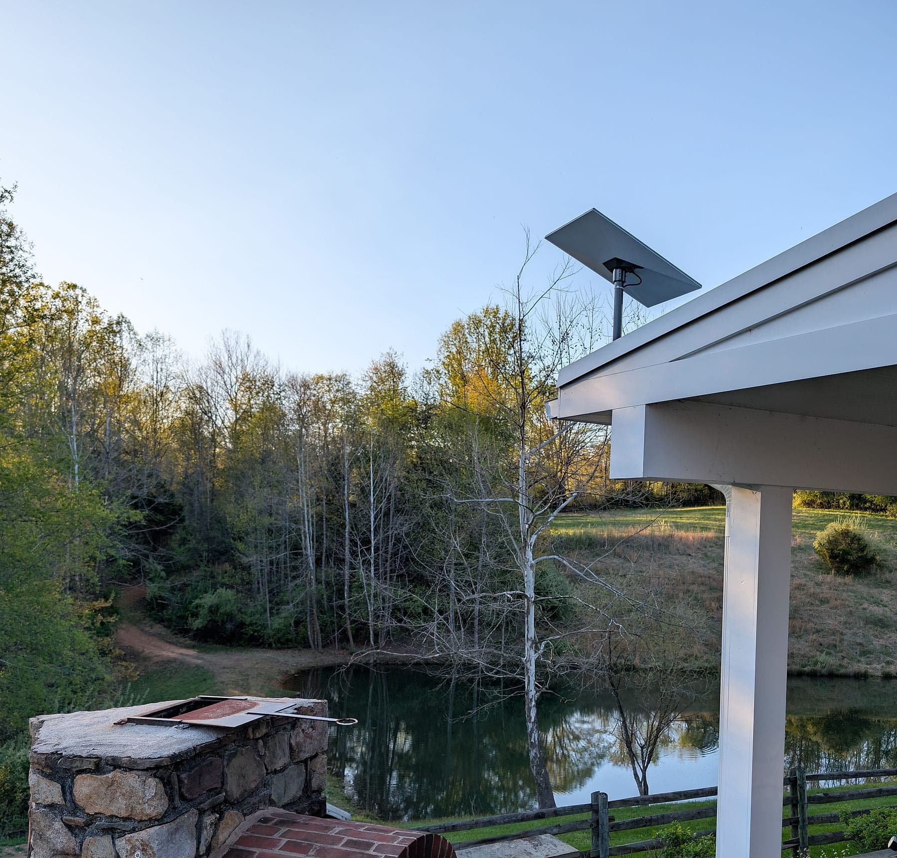 Starlink dish above the pavilion at dusk, pond and stone outdoor kitchen in the foreground
