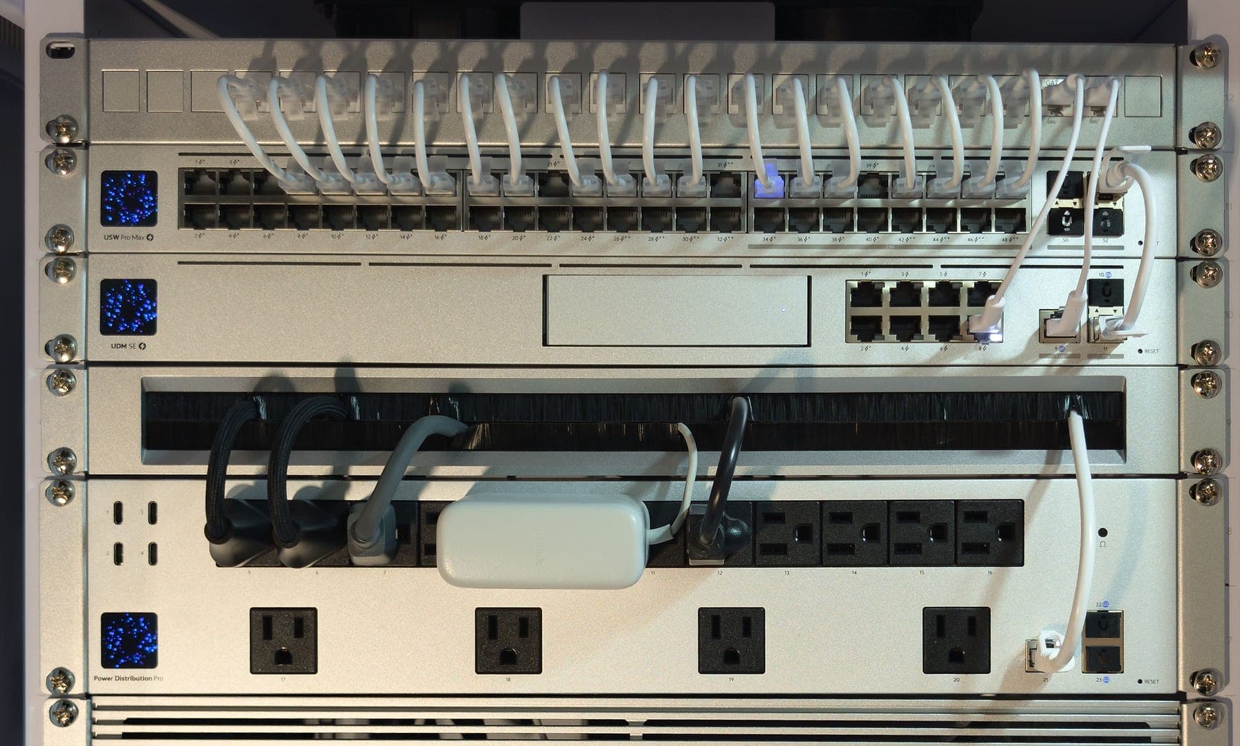 Detail of the rack core — dressed patch leads from the panel into the USW Pro Max 48 PoE, the UDM SE below it, a brush panel, and the Power Distribution Pro
