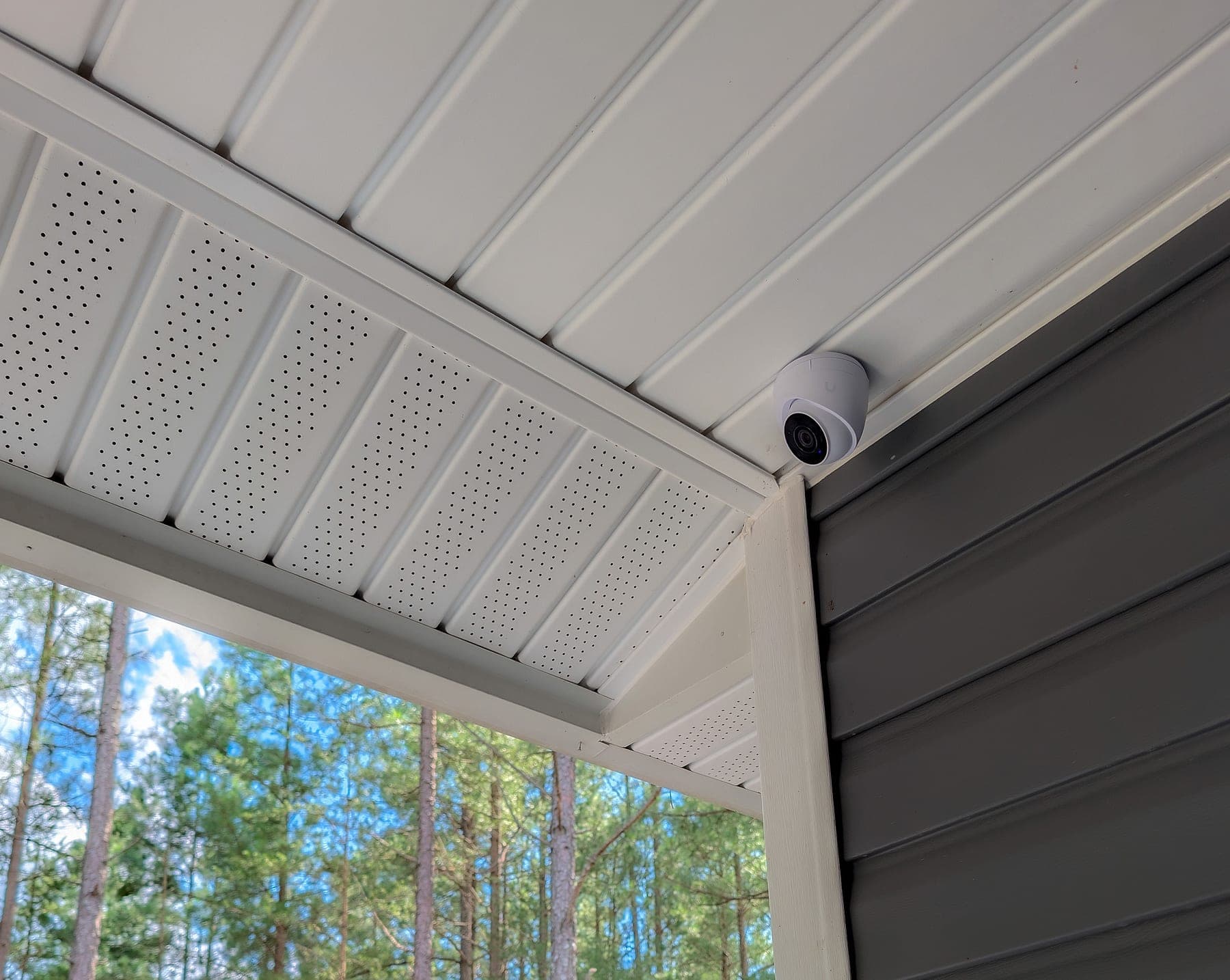 UniFi G5 Turret Ultra camera at the porch soffit corner with pine trees beyond