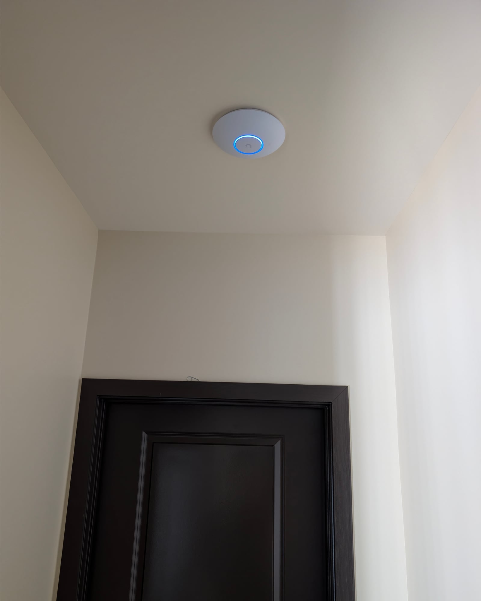 Round white ceiling-mounted access point with a blue status ring, above a dark interior door in a finished home in Partlow, Virginia